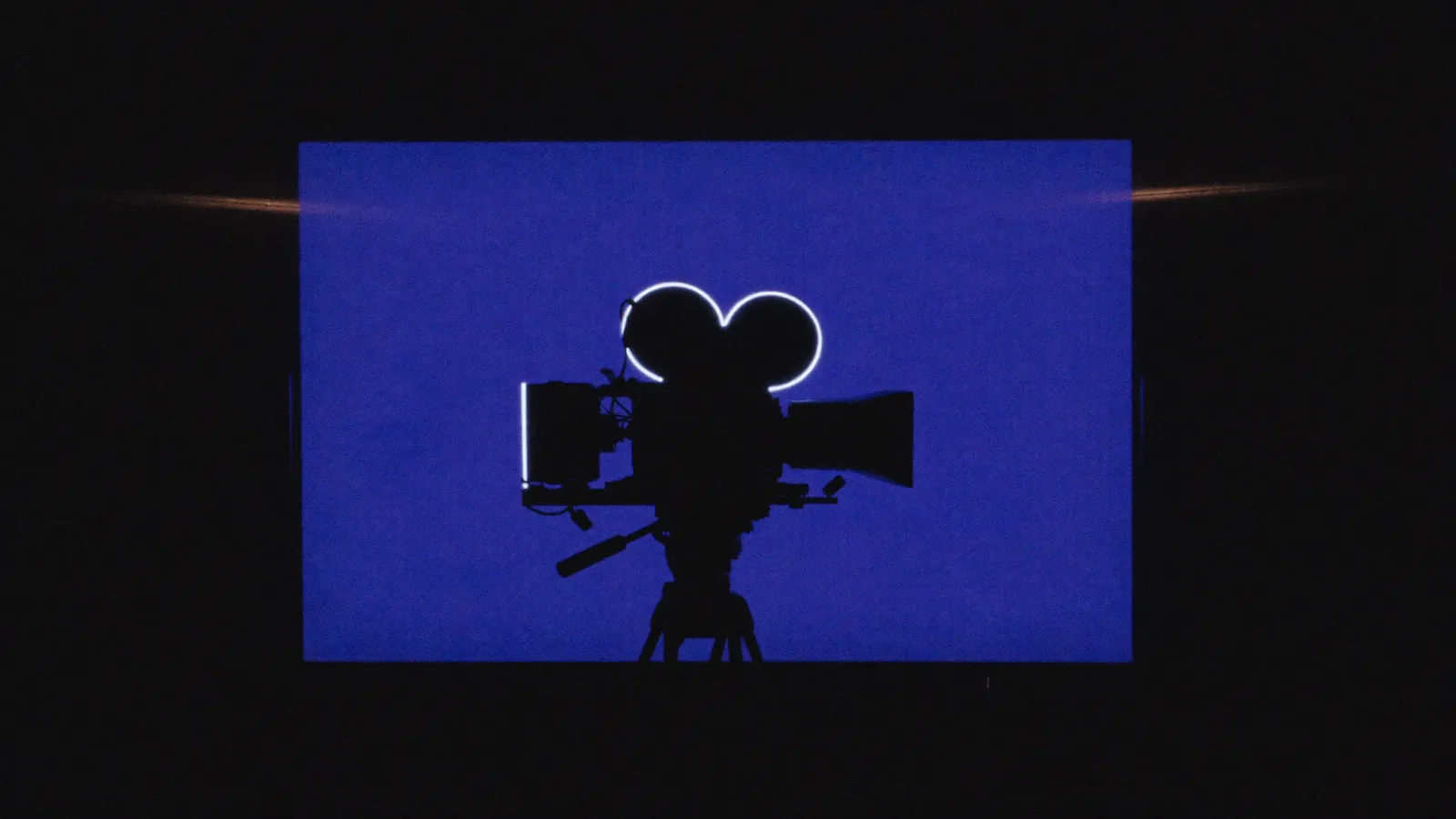 Sample — a silhouetted cinema camera lit by an indigo LED panel in a dark studio.