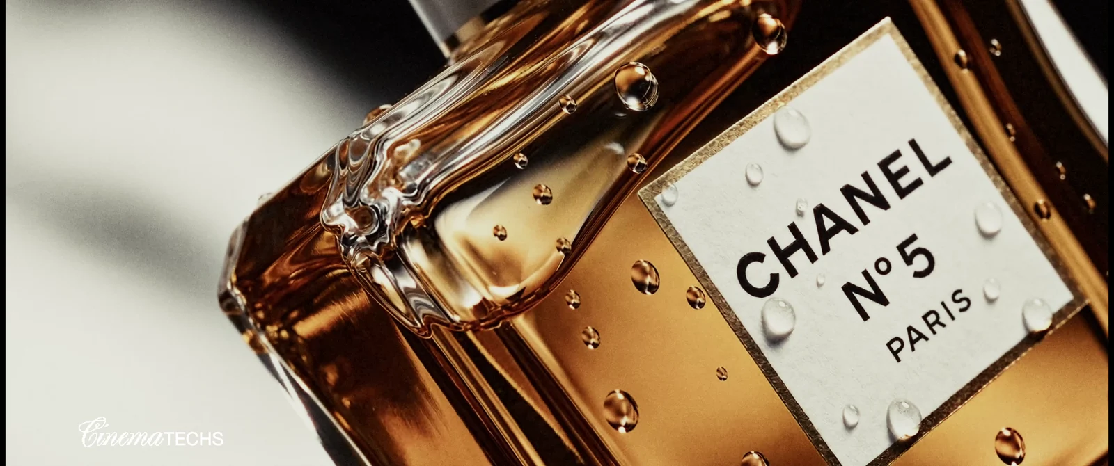 Extreme macro of a fragrance bottle: amber liquid, water droplets on glass, and a crisp printed label.