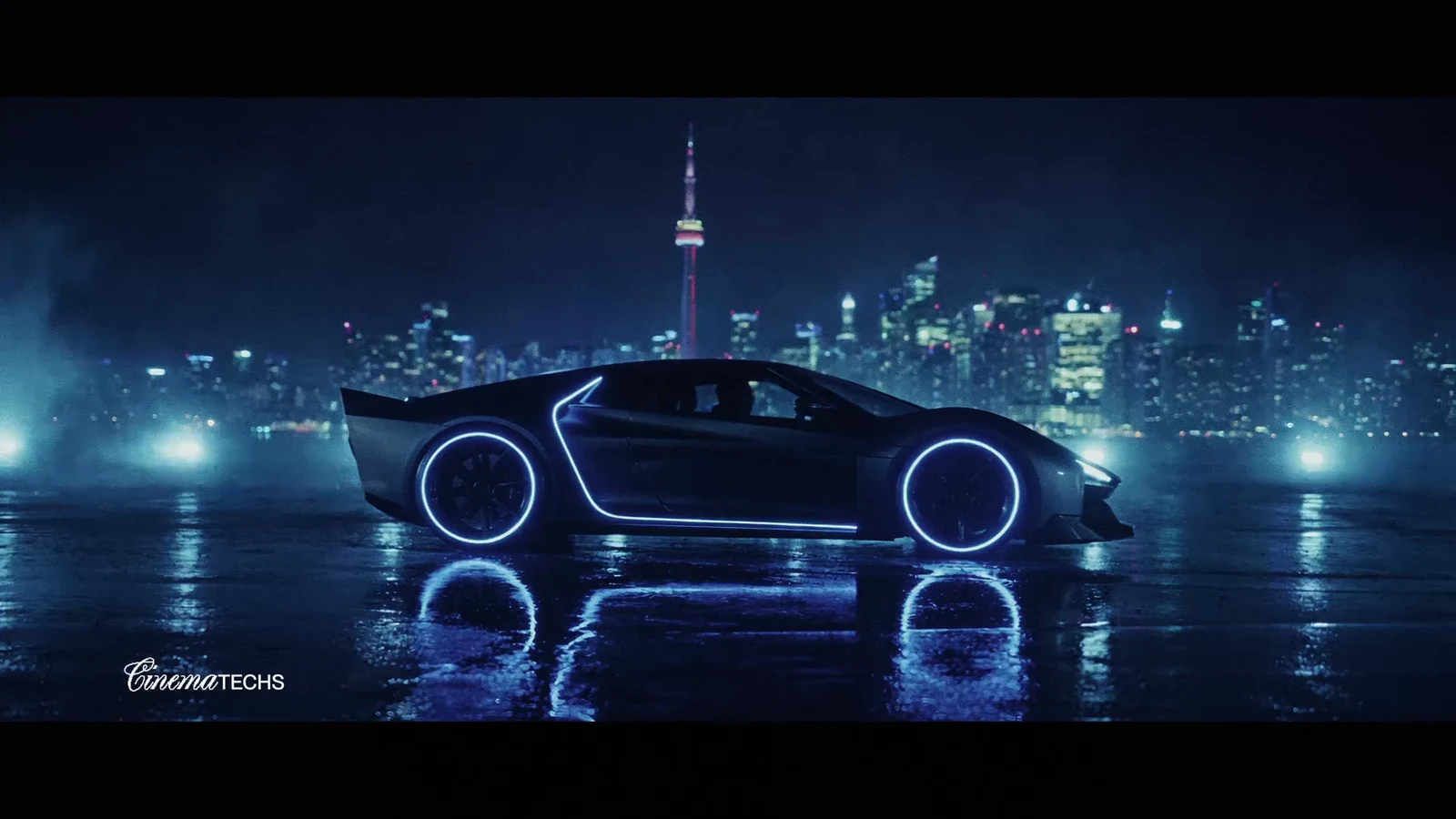 Chrome concept car in a front three-quarter view on a wet, reflective street with soft city bokeh behind it.