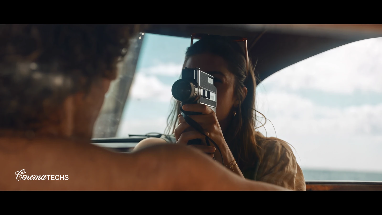 A woman raises a 35mm compact camera through an open car window, the dim interior and the bright exterior both held.