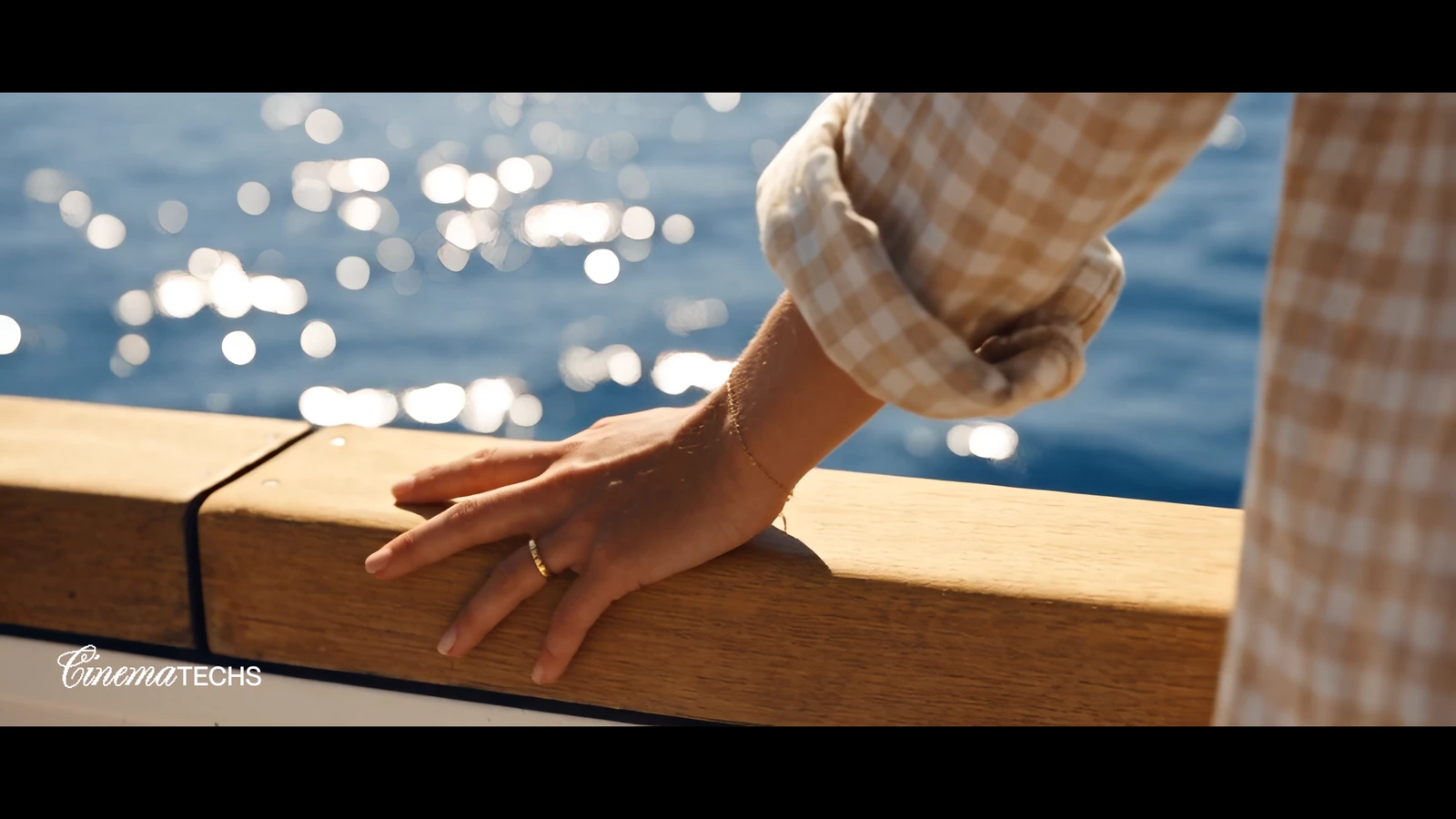 A hand resting on a varnished timber rail over sparkling water.
